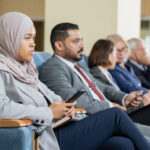 Group of serious multi-ethnic business people sitting in auditorium and listening to presentation at conference